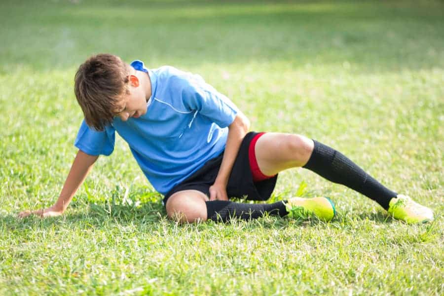 Teenage soccer player sitting down on field and holding back of thigh