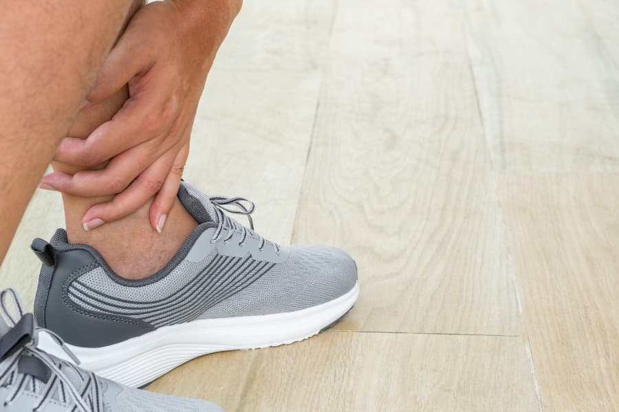 Person crouched down holding ankle in pain