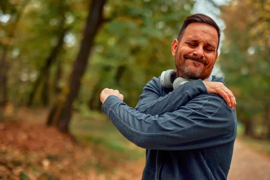 Young bearded runner with headphones grabbing shoulder in woods