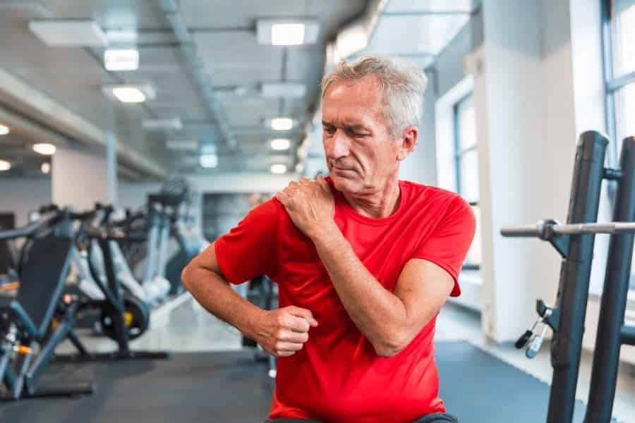 Older person suffering from shoulder pain at gym